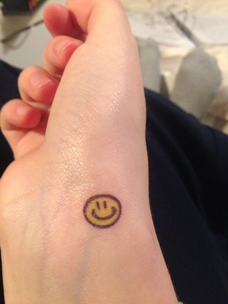 Hình tattoo mặt cười ở tay màu vàng